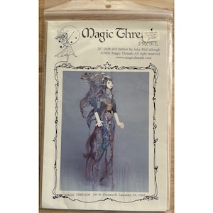 May include: A package for a cloth doll pattern labeled "Magic Threads Smoke." The pattern is for a 26-inch doll. The image on the package shows a doll with long, flowing hair and a detailed, ornate dress in shades of blue and purple.