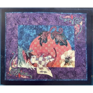 May include: A rectangular fabric wall hanging featuring a central scene of a cat resting under a large red checkered sun. The piece includes purple borders with swirling quilted patterns, decorative green vine motifs, and a white floral accent.