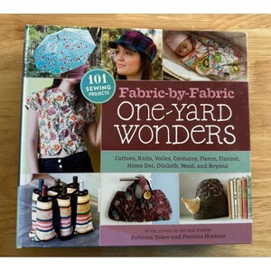May include: A book cover titled "Fabric-by-Fabric One-Yard Wonders" with images of sewing projects. The cover features a woman wearing a floral shirt, a baby wrapped in fabric, and various craft projects. The book promises 101 sewing projects.