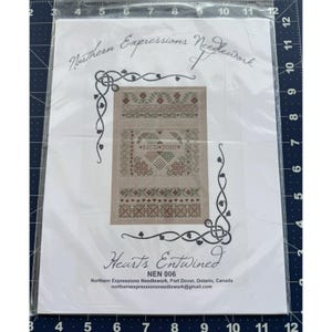 May include: A cross-stitch pattern titled "Hearts Entwined" by Northern Expressions Needlework. The design features a central heart motif, decorative borders, and the text "NCD 2010." The pattern is packaged in a clear plastic sleeve.