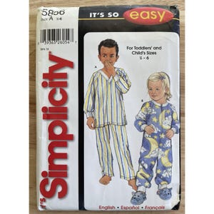 Könnte beinhalten: Simplicity Schnittmuster für Kinderpyjamas. Das Muster zeigt zwei Pyjama-Designs: ein gestreiftes zweiteiliges Set und einen blauen Overall mit Mond- und Sterngrafiken. Das Muster ist für die Größen 1/2-6.