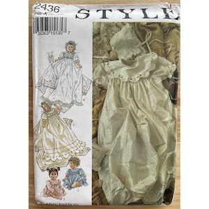 Puede incluir: Un patrón de costura vintage para ropa de bebé, con ilustraciones de un vestido de bebé, un gorro y otras prendas. El patrón incluye múltiples opciones de tamaño e instrucciones detalladas para crear los conjuntos. La portada es de color blanquecino con la palabra "STYLE" en la parte superior.