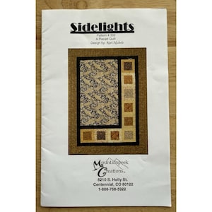 May include: A printed quilt pattern named "Sidelights" with a pieced design. The quilt features a central panel with a paisley pattern in gold and brown, framed by a dark border. The pattern includes the designer's name and company information.