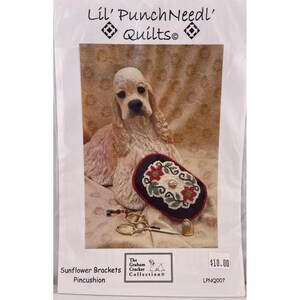 May include: A craft kit package featuring a Cocker Spaniel statue, a pincushion with red and white floral designs, and gold-colored scissors. The package is labeled "Lil' PunchNeedl' Quilts" and "Sunflower Brackets Pincushion."