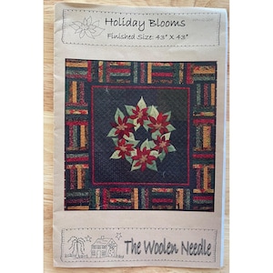 May include: A quilt pattern booklet titled Holiday Blooms by The Woolen Needle. The cover features a dark square quilt with a central wreath of red poinsettia flowers and green leaves, surrounded by a multi-colored striped border. Size 43" x 43".