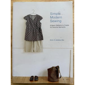 May include: A book cover titled "Simple Modern Sewing" displays a patterned top and shorts hanging on a wall. A brown tote bag and sandals are at the bottom. The book promises 8 basic patterns to create 25 garments.