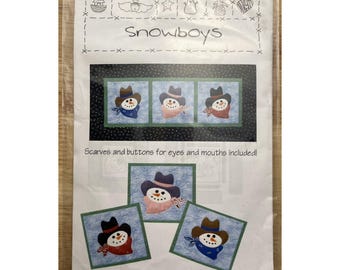 Könnte beinhalten: Eine Packung für ein Quiltprojekt mit dem Titel "Snowboys". Die Packung zeigt ein Design von Schneemännern mit Hüten und Schals. Der Text "Scarves and buttons for eyes and mouths included!" ist ebenfalls sichtbar.