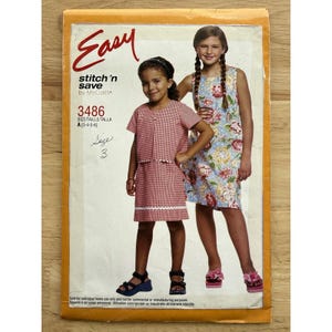 Puede incluir: Un patrón de costura vintage titulado "Easy stitch 'n save by McCall's", número 3486. El patrón presenta a dos niñas, una con un vestido de cuadros rojos y la otra con un vestido floral. La talla es A (3-4-5-6).