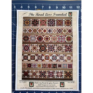 Pode incluir: Um padrão de colcha intitulado "The Road Less Traveled" com vários desenhos de blocos geométricos em tons de castanho, vermelho e creme. O padrão mede 133 cm x 175 cm e inclui texto de "From my heart to your hands".