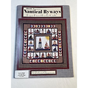 May include: A book cover titled "Nautical Byways" featuring a quilt design with nautical themes. The quilt design includes sailboats, anchors, and lighthouses in various colors. The cover has a checkered border and text that reads "by Eileen Chapman."