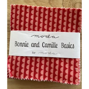 Peut inclure: Un paquet de carrés de tissu à motifs rouges et blancs. Le tissu présente un motif de festons répétitif. Une étiquette blanche indique "Bonnie and Camille Basics for moda."