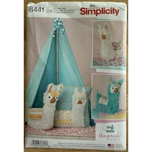 Puede incluir: Un patrón de costura Simplicity con peluches de llama y un tipi. El patrón incluye instrucciones para crear llamas de peluche en blanco y turquesa, junto con un pequeño tipi en tonos azules. El patrón es de Gingercake.