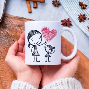 May include: White ceramic mug with a black and white illustration of a mother and daughter holding a red heart. The text "Love you" is written on the mug.