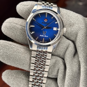Puede incluir: Reloj Rado Golden Horse de acero inoxidable con esfera azul. Cuenta con una ventana de fecha a las 3 en punto y un brazalete plateado. La esfera muestra el logotipo de Rado y la inscripción "Golden Horse". Diseño clásico.