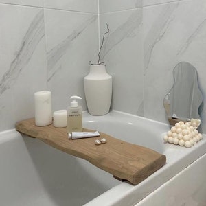 May include: A wooden bath tray with a white candle, a bottle of body wash labelled "Simply Water", a tube of hand cream, and two pearl-like bath beads. The tray is in a white bathtub with a white ceramic vase and a decorative mirror.