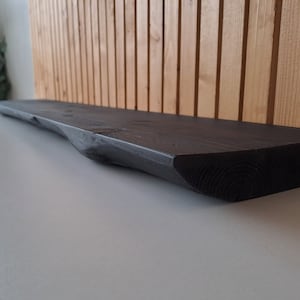 May include: A dark stained wooden shelf with a natural edge, perfect for displaying decorative items or plants.