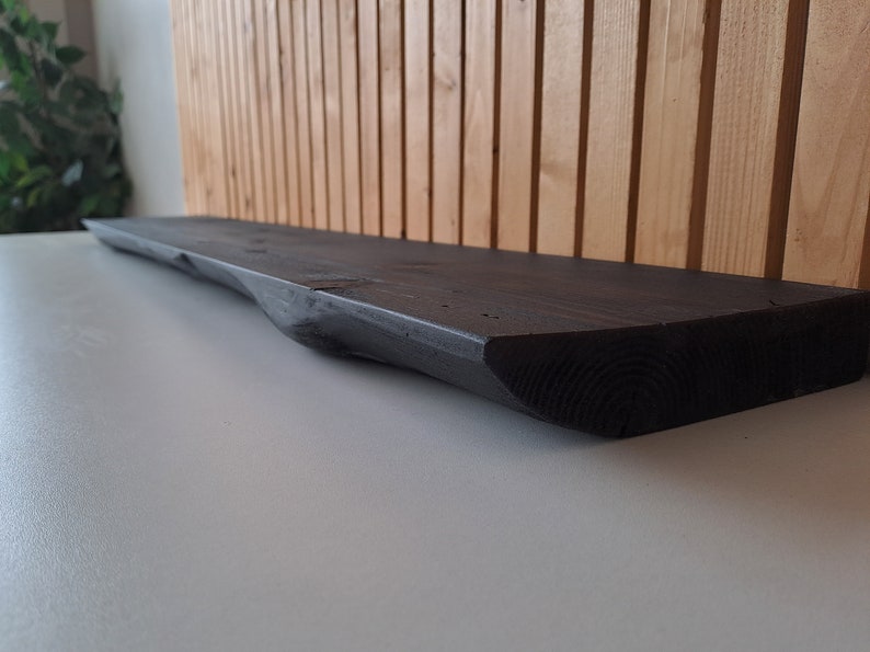 May include: A dark stained wooden shelf with a natural edge, perfect for displaying decorative items or plants.
