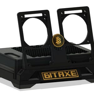 May include: A black Bitaxe Bitcoin mining device featuring a rectangular base with a honeycomb-patterned top surface. Two vertical fan mounts extend upward, with a circular gold Bitcoin logo emblem centered between them and a gold Bitaxe nameplate.