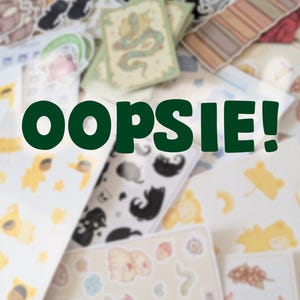 Könnte beinhalten: Eine Sammlung von Aufklebern und Karten mit verschiedenen Designs, darunter Katzen, Pilze und ein Drache. Das Wort "OOPSIE!" ist in großen, dunkelgrünen Buchstaben über das Bild geschrieben. Die Aufkleber und Karten sind verstreut.
