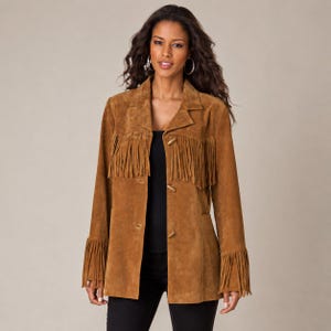 May include: A tan suede jacket featuring long fringe detailing across the chest and on the cuffs of the sleeves. The jacket has a notched collar, a button-front closure with three toggle-style buttons, and long sleeves, worn over a black top.
