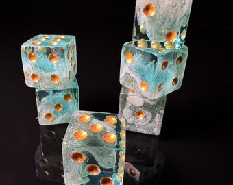 May include: Six clear resin dice with a blue and white swirl design and gold-colored dots. The dice are stacked on a reflective black surface, creating a visually appealing arrangement. These dice are perfect for tabletop games.