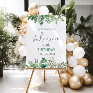 May include: Welcome to Valerie's 40th Birthday sign with green watercolor leaves and greenery. The sign is on a wooden easel and surrounded by gold and white balloons.