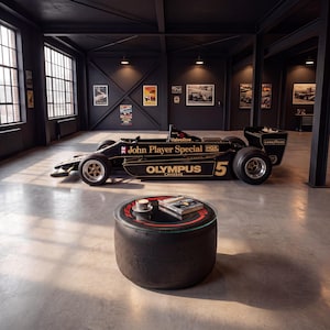 Op de afbeelding: Een ronde salontafel gemaakt van een zwarte raceband met een glazen blad, waarop een klein wit kopje en een boek staan. Op de achtergrond staat een zwarte John Player Special Formule 1-raceauto met gouden belettering tentoongesteld.