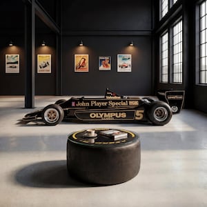 Può includere: Un'auto da corsa di Formula 1 nera e oro con il numero 5 e i marchi John Player Special, Olympus Cameras e Valvoline. In primo piano, un tavolino circolare con piano in vetro, una tazzina bianca e un libro.