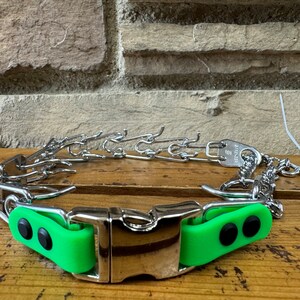 K&ouml;nnte beinhalten: Ein silbernes Stachelhalsband mit gr&uuml;ner Gummibeschichtung und einer silbernen Schnalle. Das Halsband hat ein Etikett mit der Aufschrift "Premier".