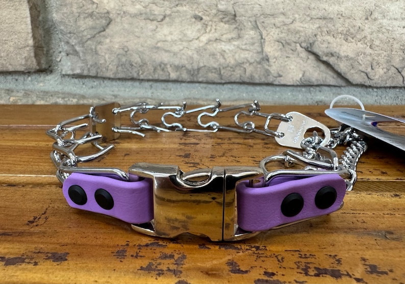K&ouml;nnte beinhalten: Ein silbernes Stachelhalsband mit einer violetten gepolsterten Schnalle. Das Halsband besteht aus Metallgliedern und hat einen D-Ring zum Anbringen einer Leine.