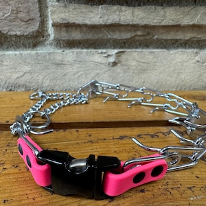 Könnte beinhalten: Ein pinkfarbenes und schwarzes Hundehalsband mit einem silbernen Kettenglieddesign. Das Halsband hat einen Schnallenverschluss und ist aus strapazierfähigen Materialien gefertigt.