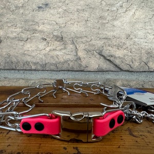 K&ouml;nnte beinhalten: Ein silbernes Stachelhalsband mit einer rosa gepolsterten Schnalle. Das Halsband besteht aus Metallgliedern und hat eine gepolsterte Schnalle f&uuml;r Komfort.