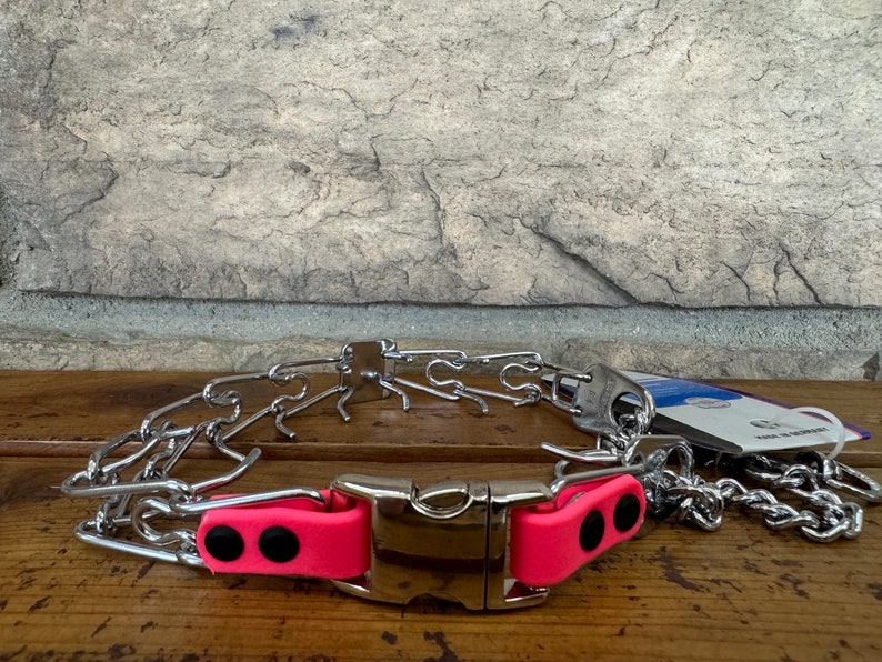 K&ouml;nnte beinhalten: Ein silbernes Stachelhalsband mit einer rosa gepolsterten Schnalle. Das Halsband besteht aus Metallgliedern und hat eine gepolsterte Schnalle f&uuml;r Komfort.