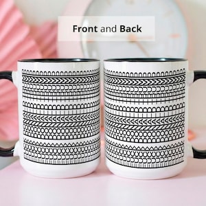 May include: Two white ceramic mugs with black handles and rims. Each mug features a black and white geometric pattern. The text "Front and Back" is visible above the mugs. The mugs are on a pink surface.