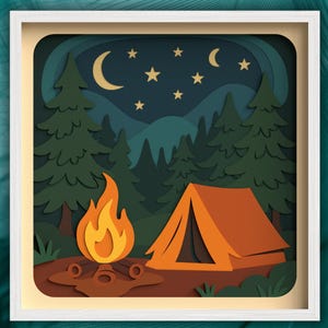 May include: A framed paper art piece depicting a camping scene. An orange tent sits near a campfire with flames, under a night sky with a crescent moon and stars. Green trees and mountains complete the outdoor theme.
