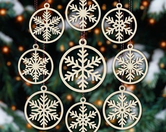 May include: Nine wooden snowflake decorations suspended by red threads. Each decoration has a snowflake design within a circular frame. The ornaments are a light beige colour, set against a blurred Christmas tree background.