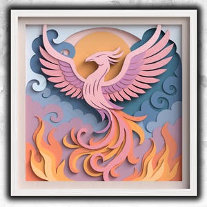 May include: A framed paper art piece depicting a phoenix rising from flames. The artwork features layers of pink, orange, and yellow paper, with a blue and purple background. The phoenix has outstretched wings and is set against a sun.