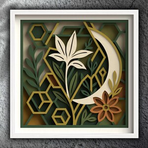 May include: A framed paper art piece with a layered design. It features a cream-colored flower, a crescent moon, and geometric shapes in shades of green and gold. A brown flower adds a touch of colour.
