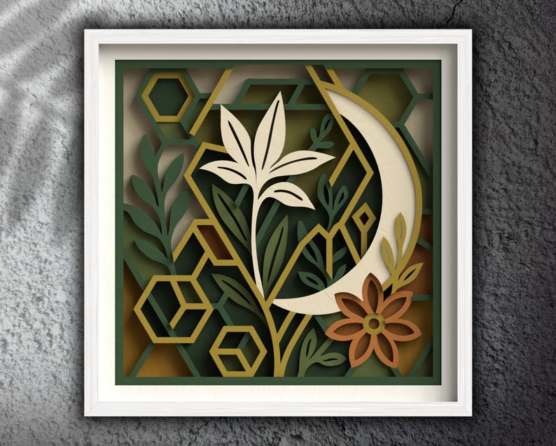 May include: A framed paper art piece with a layered design. It features a cream-colored flower, a crescent moon, and geometric shapes in shades of green and gold. A brown flower adds a touch of colour.