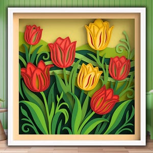 Op de afbeelding: Een ingelijst papieren kunstwerk met gelaagde rode en gele tulpen met groene bladeren en stelen. Het kunstwerk is geplaatst tegen een lichtgele achtergrond en ingelijst in een witte schaduwdoos.