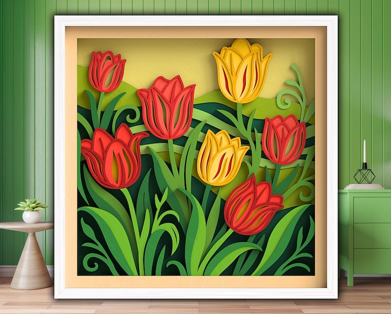 Op de afbeelding: Een ingelijst papieren kunstwerk met gelaagde rode en gele tulpen met groene bladeren en stelen. Het kunstwerk is geplaatst tegen een lichtgele achtergrond en ingelijst in een witte schaduwdoos.