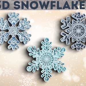May include: Three 3D paper snowflakes with intricate designs. The snowflakes are blue and white and have a layered look. The snowflakes are on a white background with a light brown wooden surface in the background.