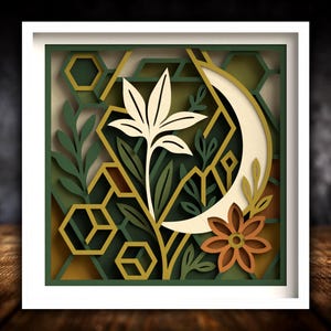 May include: A framed paper artwork with a layered botanical design. It features a cream-coloured flower, a crescent moon, and geometric shapes in green, gold, and brown. The artwork is set within a white frame.