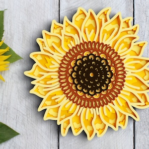 A layered sunflower design set against a gray wooden background, accented with leaves.