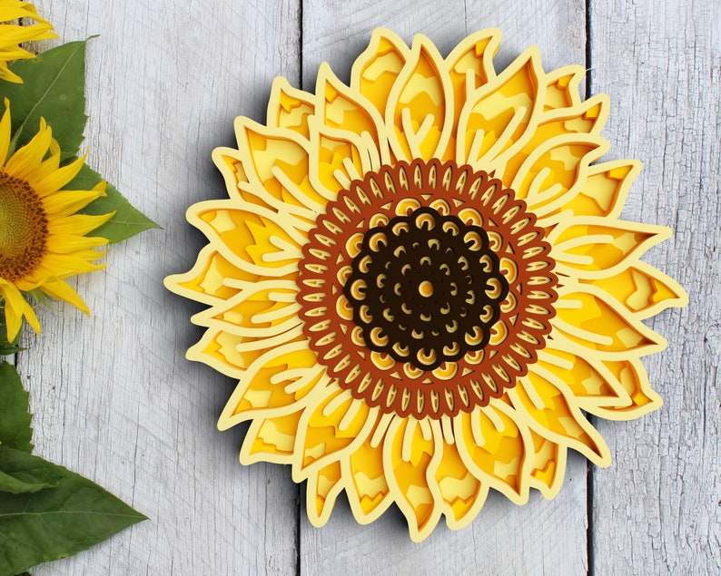 A layered sunflower design set against a gray wooden background, accented with leaves.