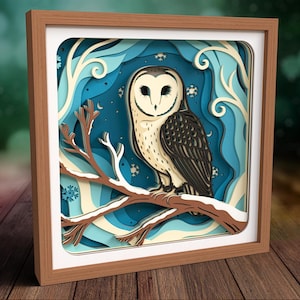 May include: A square wooden frame containing a multi-layered paper art piece featuring a barn owl perched on a snow-covered branch. The background consists of layered shades of blue and cream, depicting a winter forest scene with snowflakes.