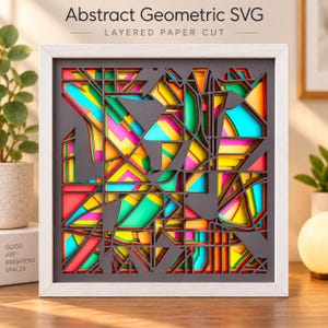 May include: A square framed wall art piece featuring an abstract geometric design with layered paper cutouts. The artwork displays a complex pattern of dark gray cutouts revealing vibrant neon yellow, pink, and turquoise layers underneath.
