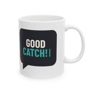 Könnte beinhalten: Ein weißer Keramikbecher mit einer schwarzen Sprechblasen-Grafik auf der Vorderseite. Innerhalb der Sprechblase ist der Text GOOD in Weiß und das Wort CATCH!! in einem leuchtenden Türkis gedruckt, mittig auf der Oberfläche des Bechers.