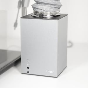 May include: A silver air purifier with a white fabric filter and a black base. The purifier has a small display with three lights and a power cord. The brand name "fnatr" is printed on the front of the purifier.