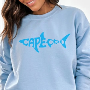 May include: A light blue sweatshirt with a blue graphic of a shark with the text "CAPE COD" inside the shark's body.